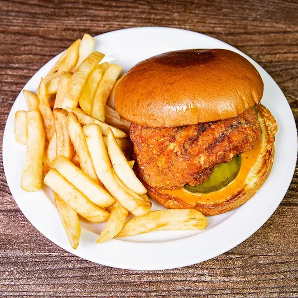 Crispy fried chicken sandwich with pickles and sauce on a bun, served with golden french fries.