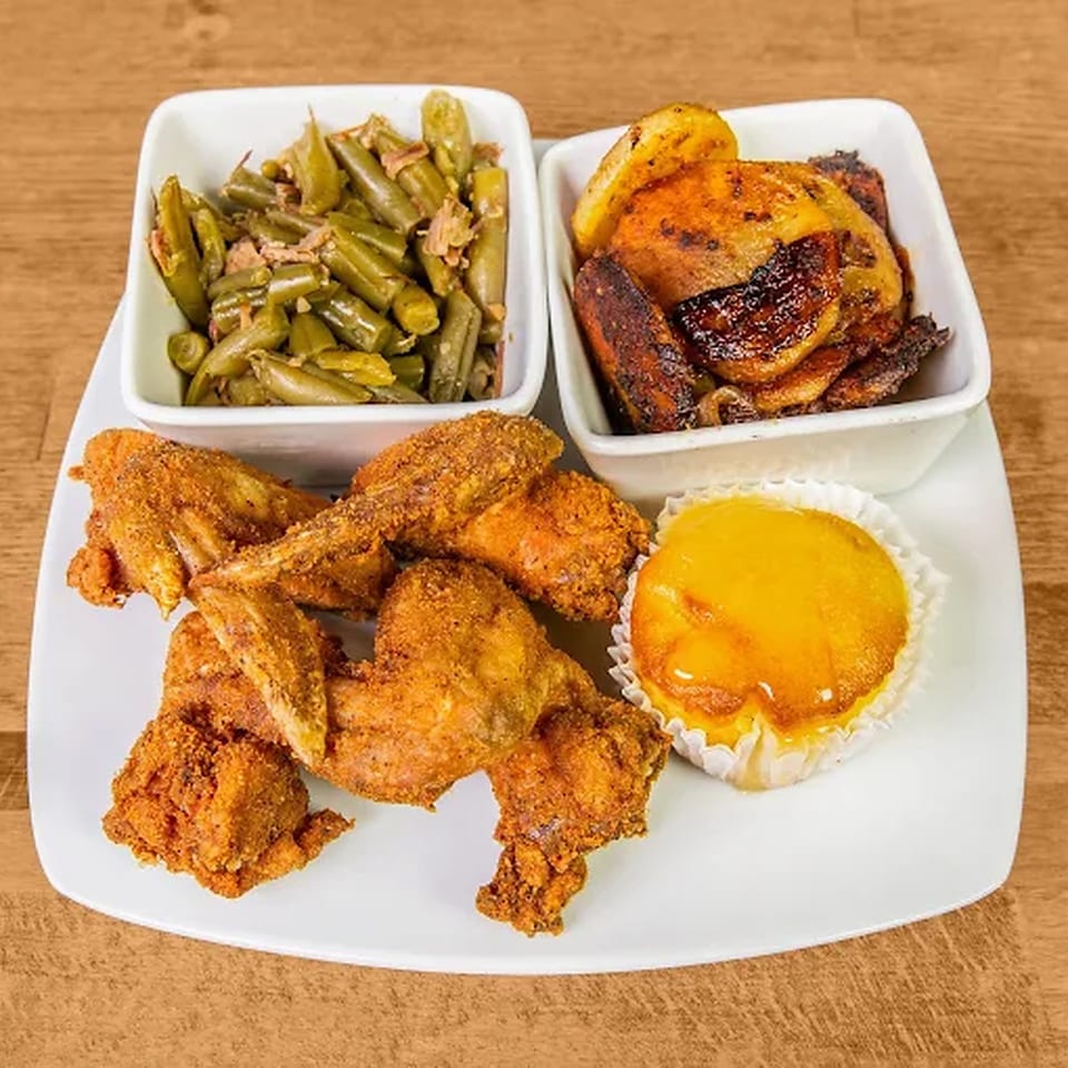 Fried chicken wings, green beans, roasted potatoes, and a small yellow cake on a white plate.