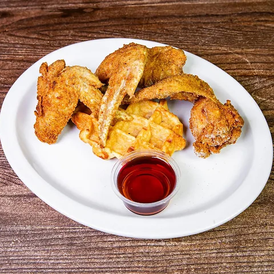 Crispy fried chicken wings and waffles with a side of syrup on a white plate.