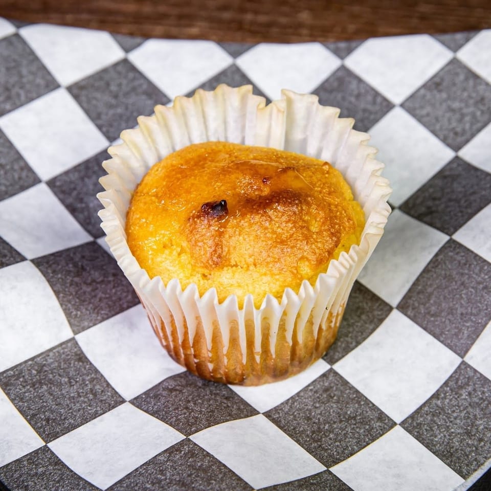 Golden brown muffin in a white paper liner, resting on black and white checkered paper.