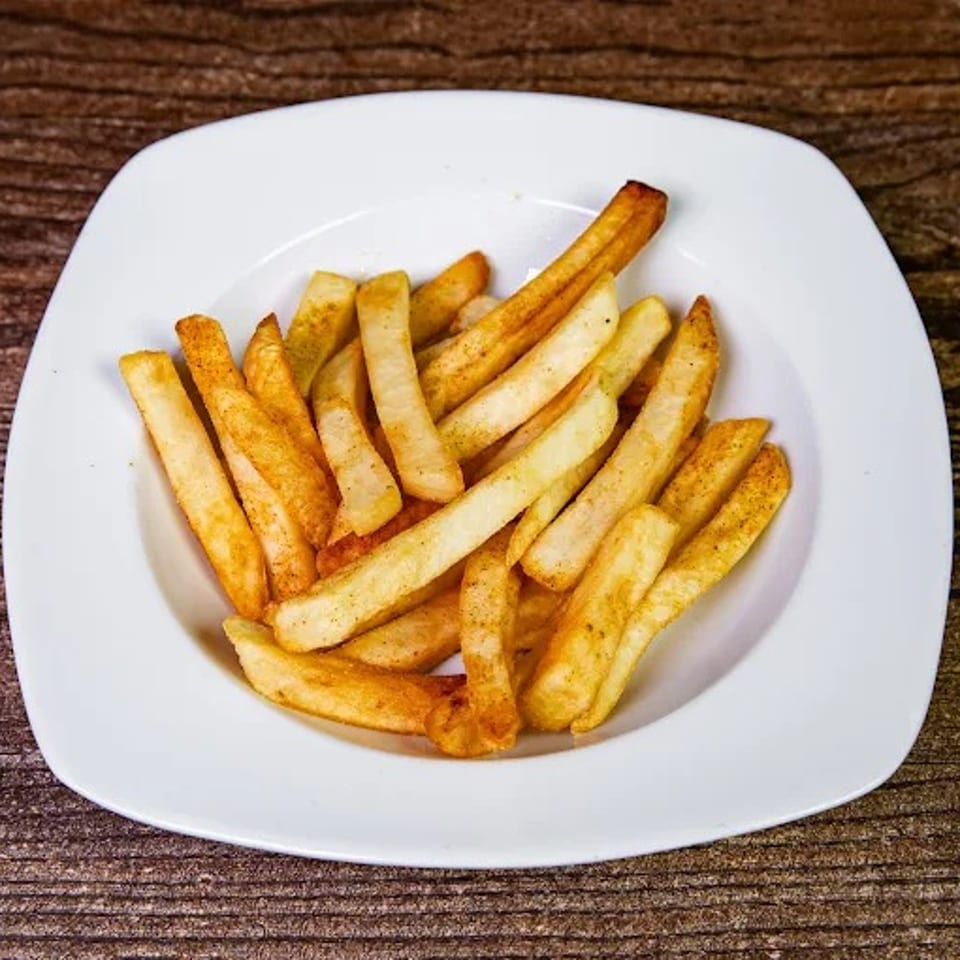 A white square plate filled with golden-brown french fries, lightly seasoned, on a rustic wooden table.